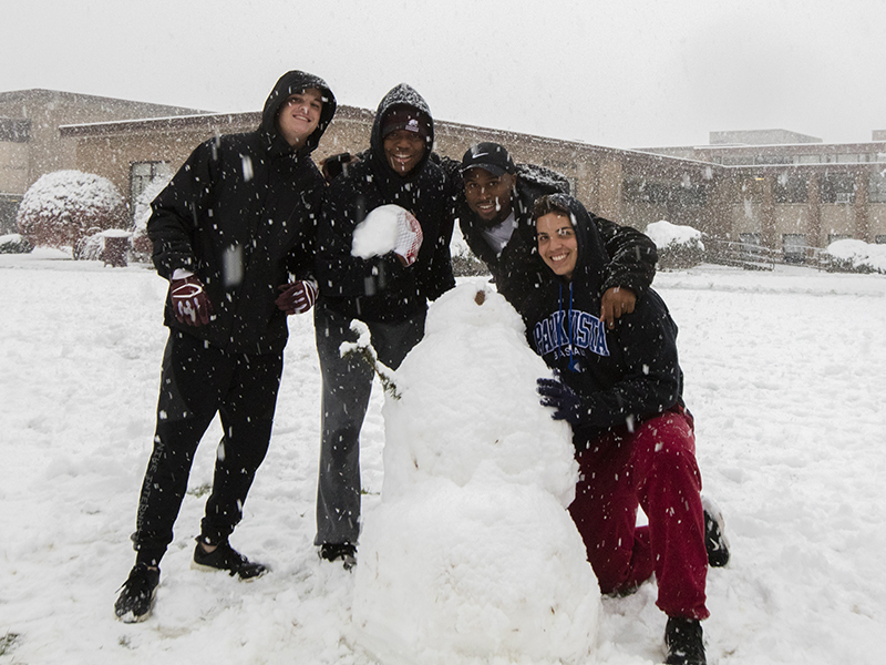 Students leaning together with a freshly made snowman on the Concordia Chicago campus